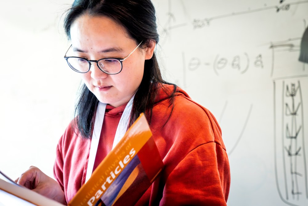 ISTA-Postdoktorandin Mengjie Zu schaut in Mehran Kardars Lehrbuch „Statistical Physics of Particles” nach.