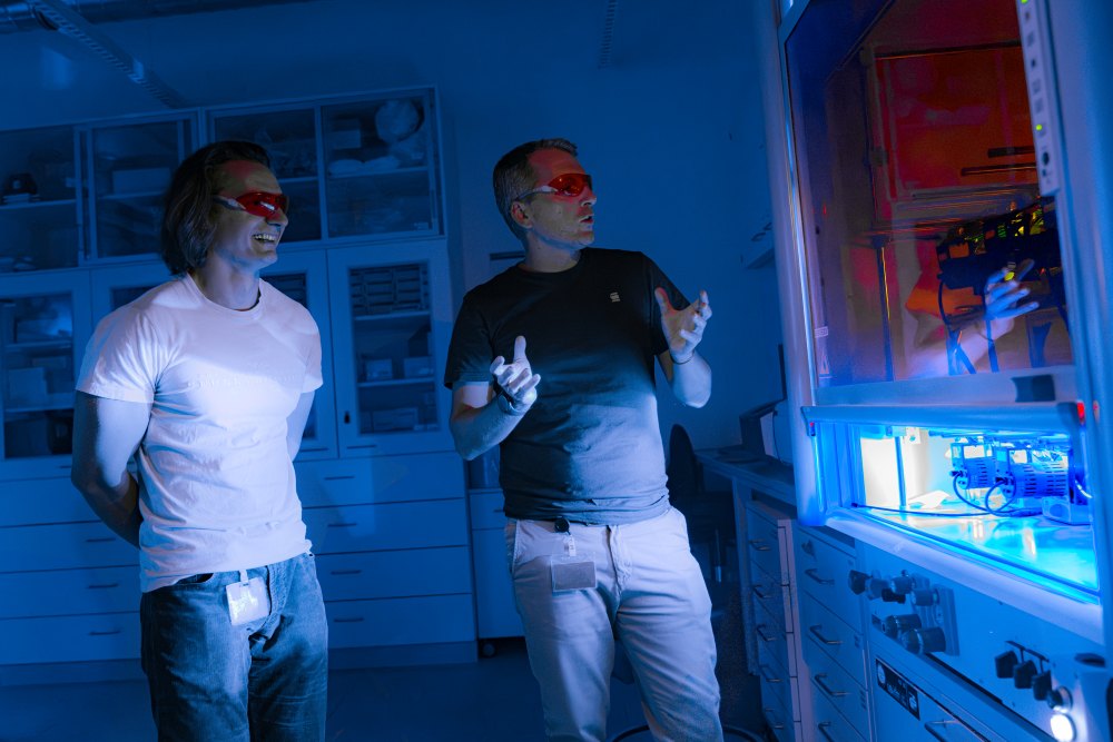 Light-activated nickel catalysis. Behind a glass pane, LED lamps shine onto small reaction vessels, activating chemical reactions.